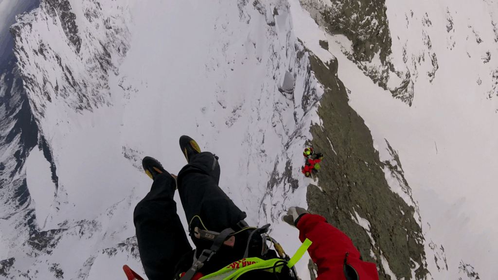 Zo záchrannej akcie HZS - záchranár HZS v podvese vrtuľníka nad pacientom s ďalším záchranárom HZS na zasneženom skalnatom teréne 