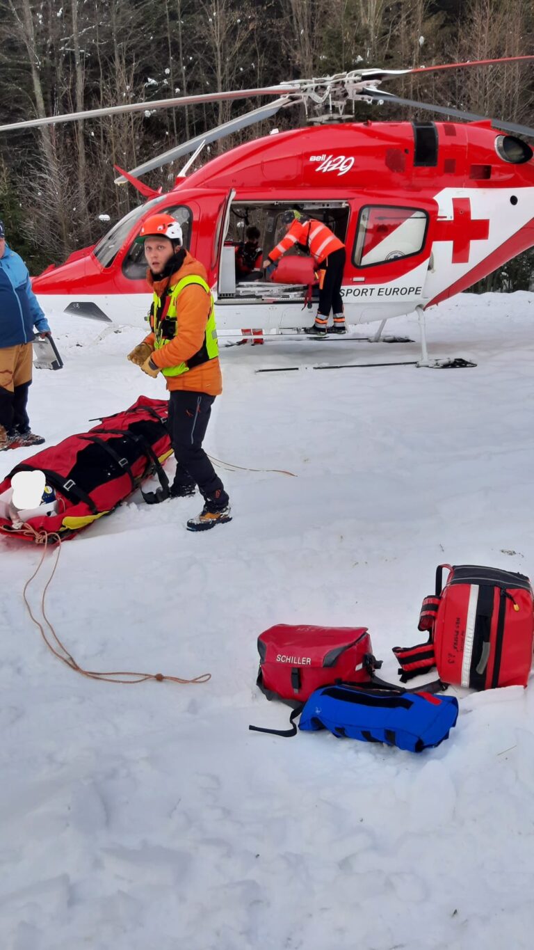 úraz na uzavretej zjazdovke v Nízkych Tatrách - záchranár HZS s pacientom na nosidlách pri odovzdaní pacienta posádke VZZS, v pozadí vrtuľník