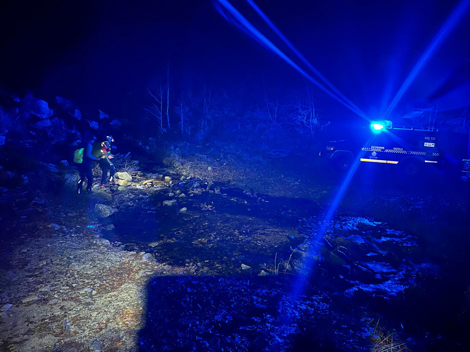 terénne vozidlo HZS so zapnutými majákmi v noci v horskom teréne, k aute smerujú záchranári HZS