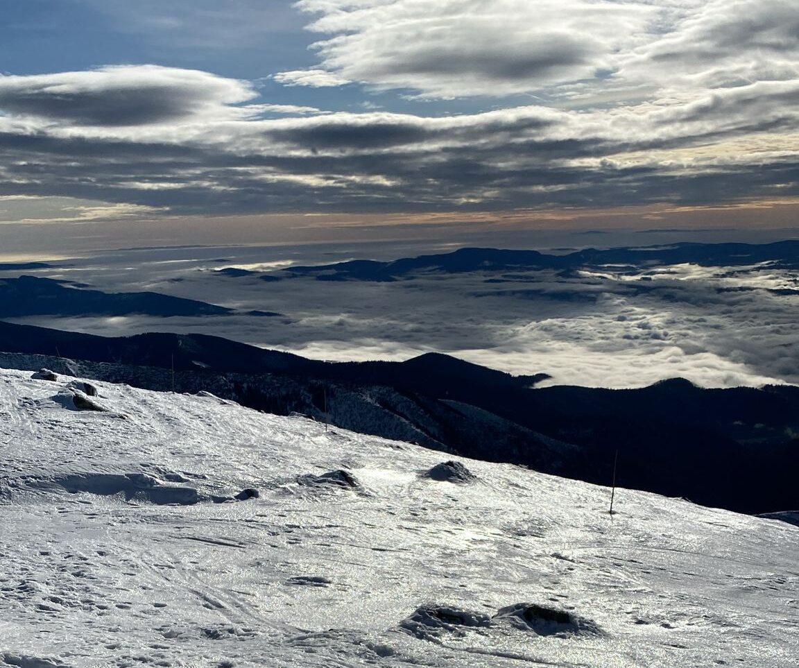 aktuálna fotografia podmienok na horách - zľadovatený sneh a vytŕčajúce skaly, v pozadí hory s inverziou