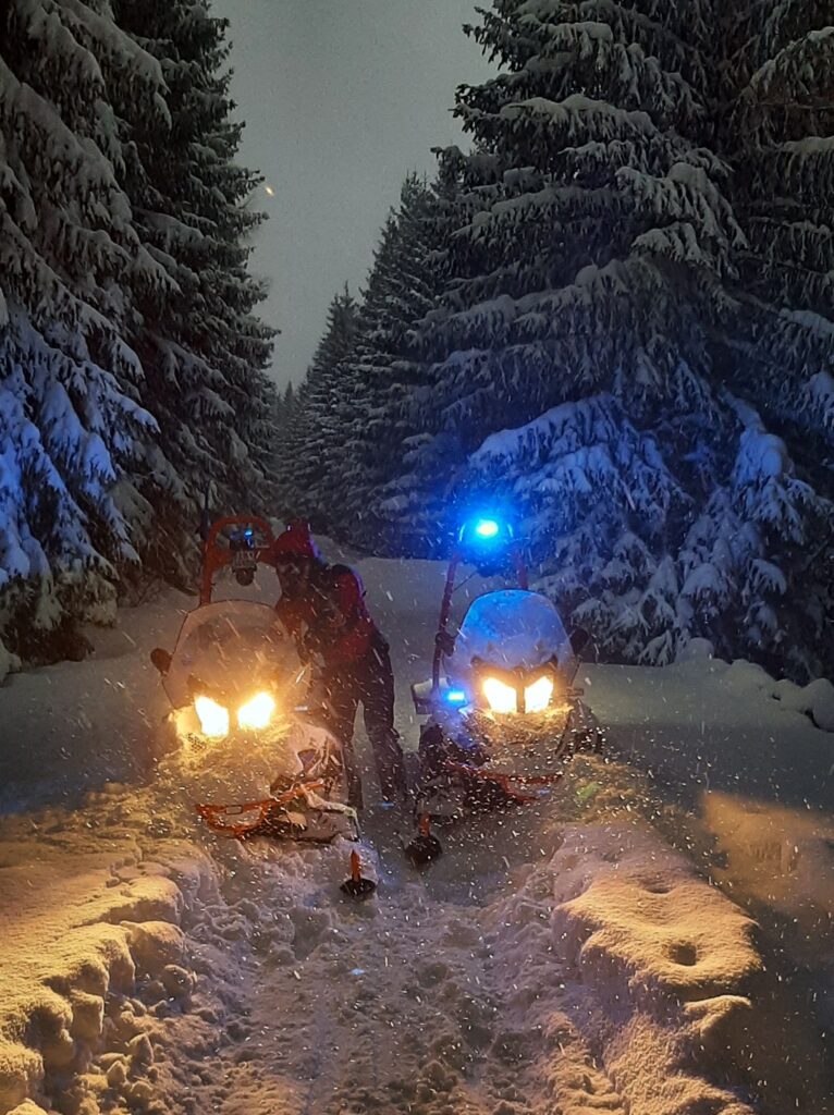 Záchranár pri naštartovaných snežných skútroch v zasneženom lese