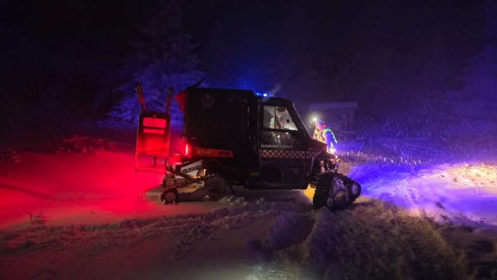 terénne vozidlo HZS na pásoch na zasneženom TZCH v noci, pri vozidle záchranár