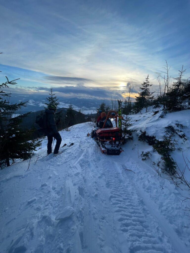 záchranár spolu s pacientom na snežnom skútri na hrebeni Nízkych Tatier, vedľa skútra záchranár HZS na lyžiach