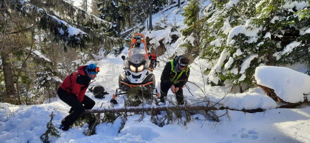 záchranári HZS prerezávajú cestu - na ceste je spadnutý strom, v pozadí snežný skúter 