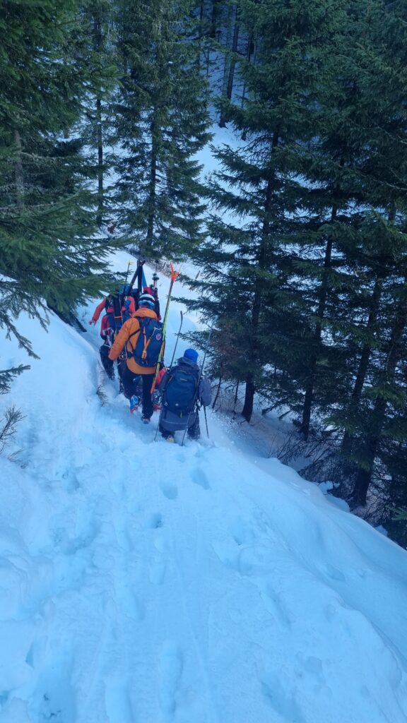 Horskí záchranári postupujú hlbokým snehom s lyžami na batohoch