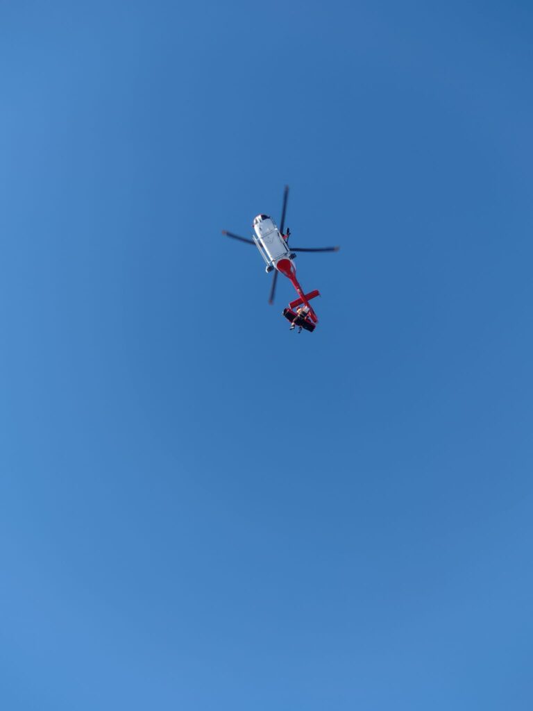 vrtnuľník ATE (bielo-červený) v podvese s lekárom VZZS a pacientkou v nosidlách, v pozadí modré nebo