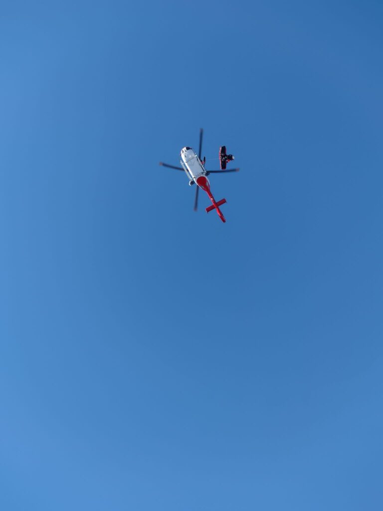 vrtnuľník ATE (bielo-červený) v podvese s lekárom VZZS a pacientkou v nosidlách, v pozadí modré nebo