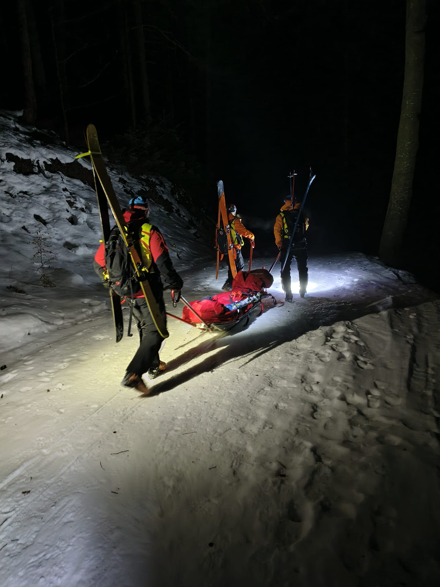 Záchranári kráčajúci so saňami v ktorých leží pacient
