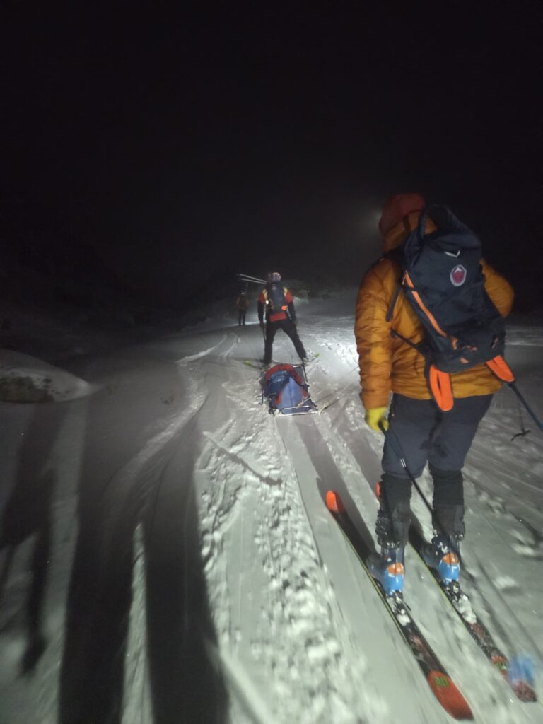 záchranári transportujú dole zasneženou Veľkou Studenou dolinou zraneného skialpinistu na saniach. Záchranári HZS zostupujú na lyžiach
