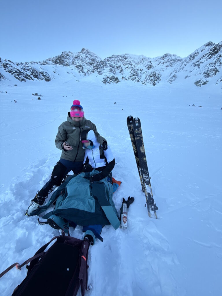 pacientka s poranenou nohou sedí zateplená pri partnerovi v zasneženej Salatínskej doline, v pozadí hrebeň Západných Tatier 