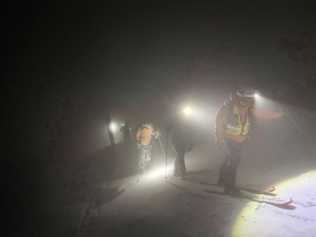 záchranári sprevádzajú uviaznutých turistov po zasneženom teréne za svetiel čeloviek