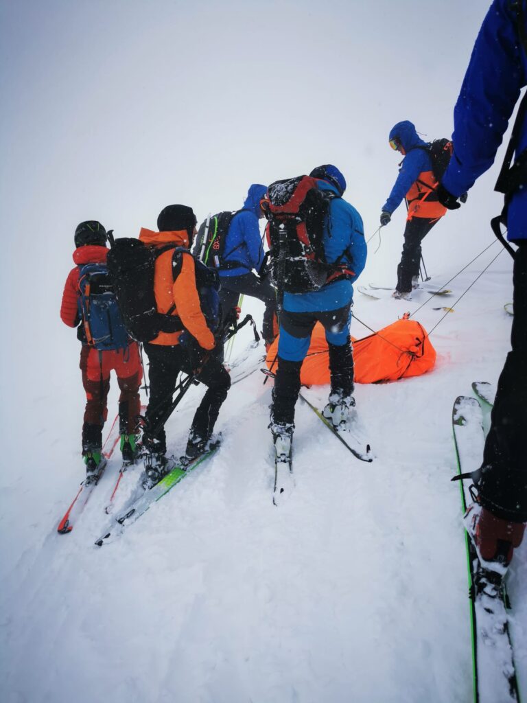 improvizovaný transport pacienta svedkami nehody na lyžiach, pacient nabalený v transportnom prostriedku zaistený lanovou technikou 
