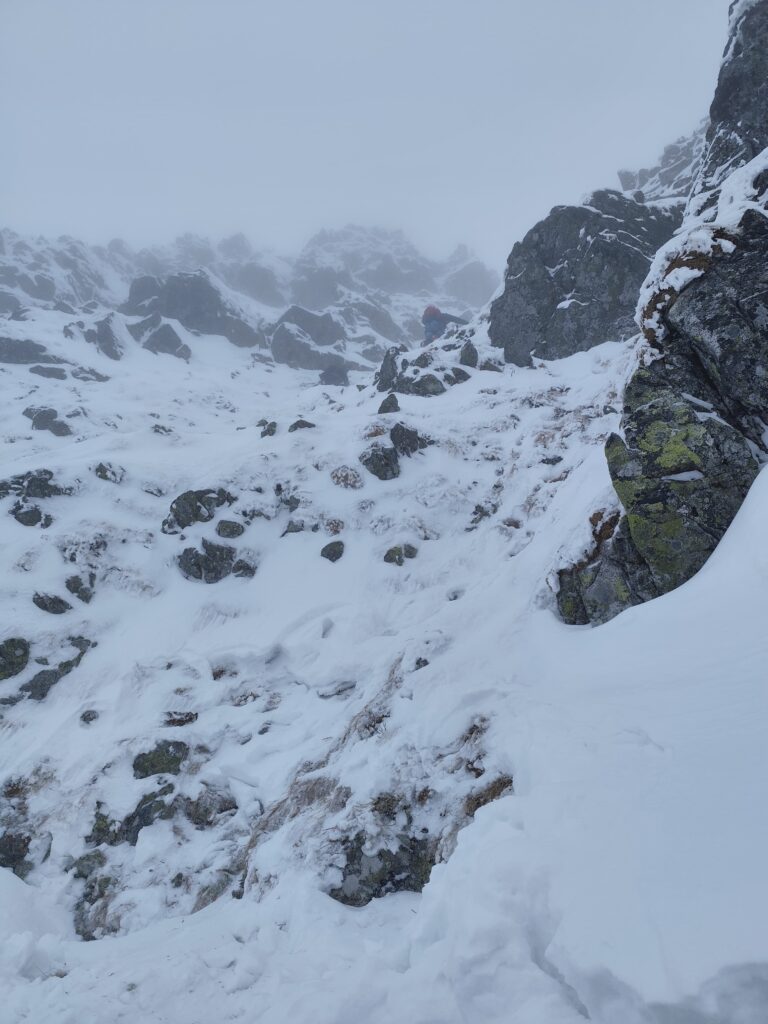 terén, v ktorom muž uviazol, strmé skalné steny pokryté snehom, v okolí hmla