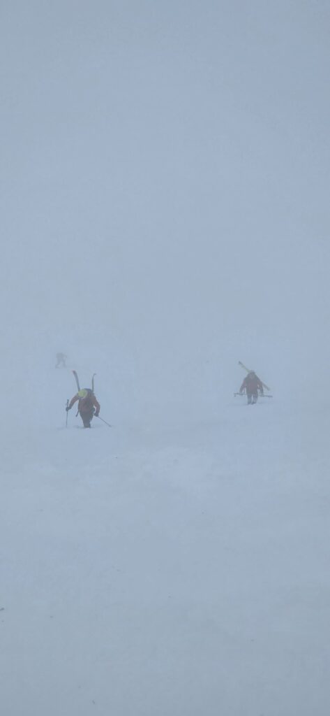 záchranári HZS vystupujú strmým svahom k uviaznutému mužovi, na chrbte majú na batohoch pripnuté lyže, zlá viditeľnosť kvôli hmle 