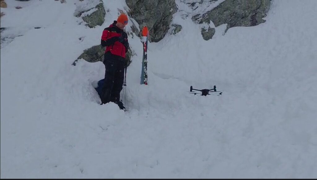 záchranár HZS rozpráva do vysielačky a vedľa neho je dron na lavínisku
