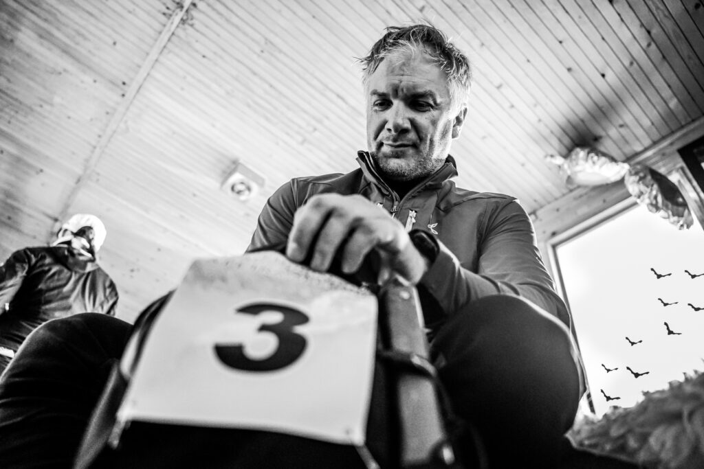 čiernobiela fotografia, účastník preteku si balí veci do svojho batoha so štartovacím číslom 