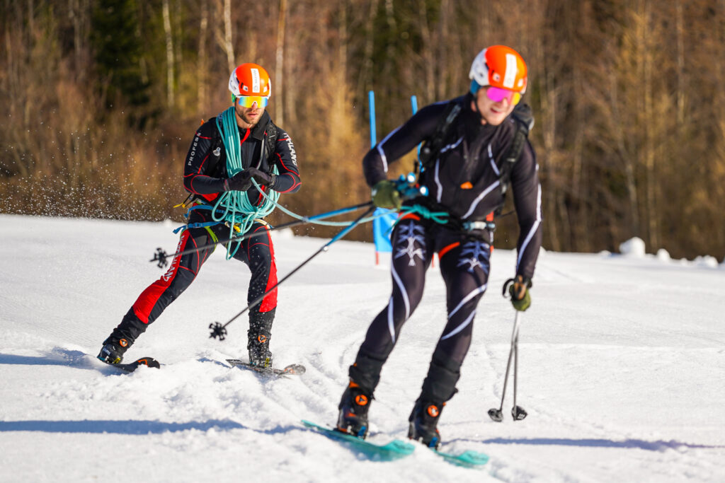 dvojica pretekárov zachytená pri obrovskom slalome naviazaná na lane obchádza bránku 