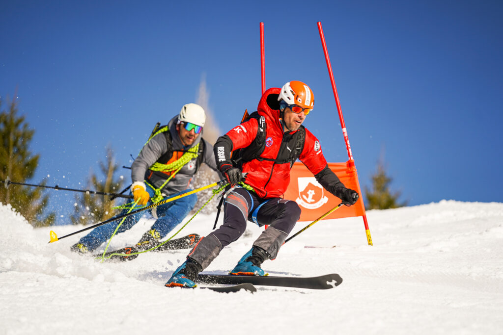 dvojica horských záchranárov naviazaných na lane medzi bránkami obrovského slalomu