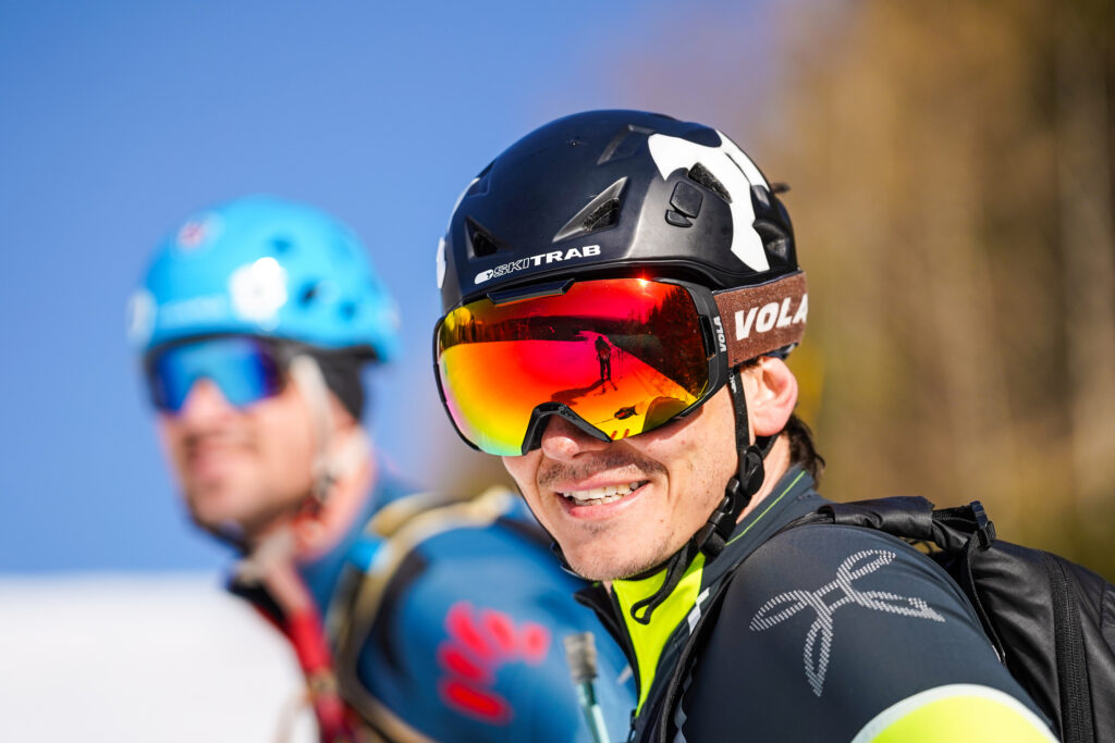 dvaja pretekári pred štartom - obaja majú na sebe prilby a lyžiarske okuliare, úsmevy a sú ožiarení slnkom 