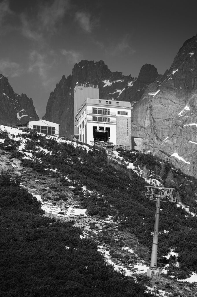 čiernobiela fotografia zachytávajúca lanovku a budovu na Skalnatom plese, v pozadí skalnaté štíty 