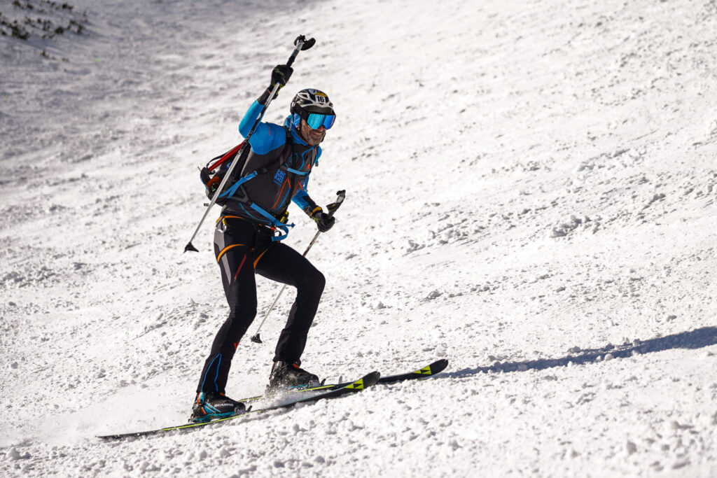 pretekár lyžujúci z Lomnického sedla, jednu ruku má hore a kýva lyžiarskou paličkou 