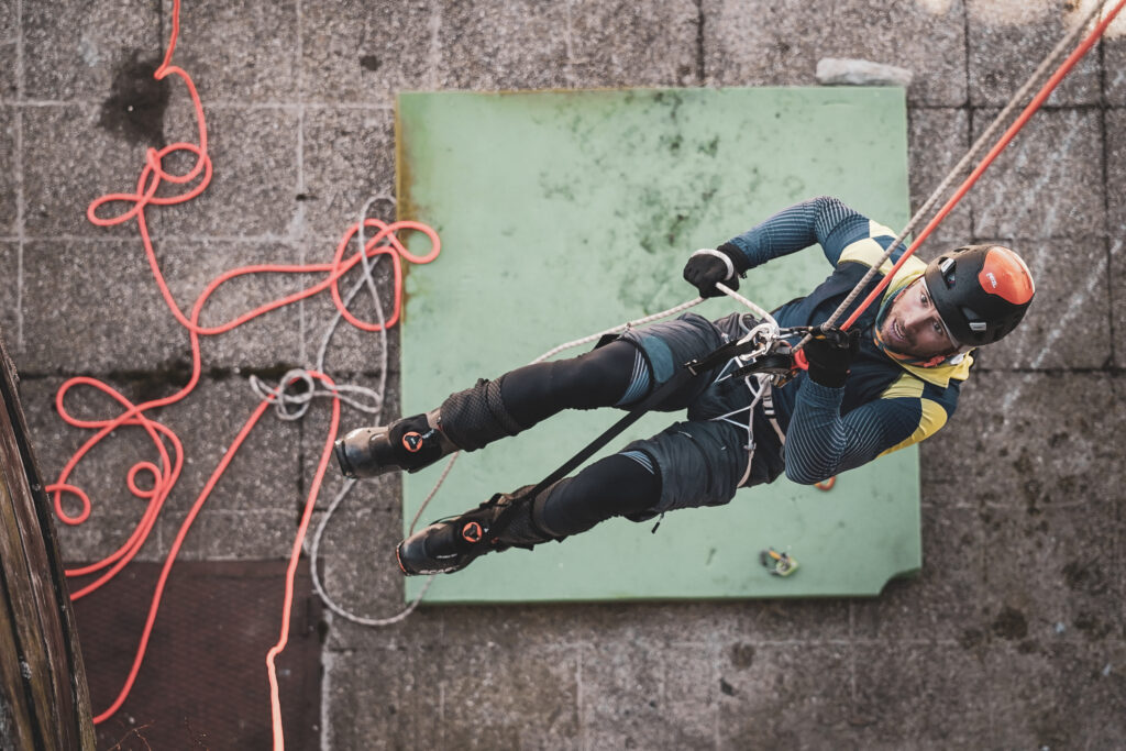 zhora odfotený pretekár naviazaný na lane vystupujúci po lane pomocou kladkostroja 