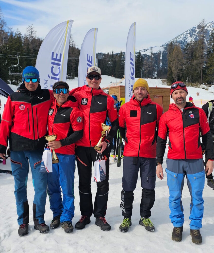 na fotke sú  šiesti záchranári HZS, ktorí sa zúčastnili preteku,  v červených služobných bundách, v rukách dvaja z nich majú trofeje za prvé miesto, zľava Erik Rabatik, Ján Šustr, Štefan Hudák, Peter Diča, Martin Matúšek  