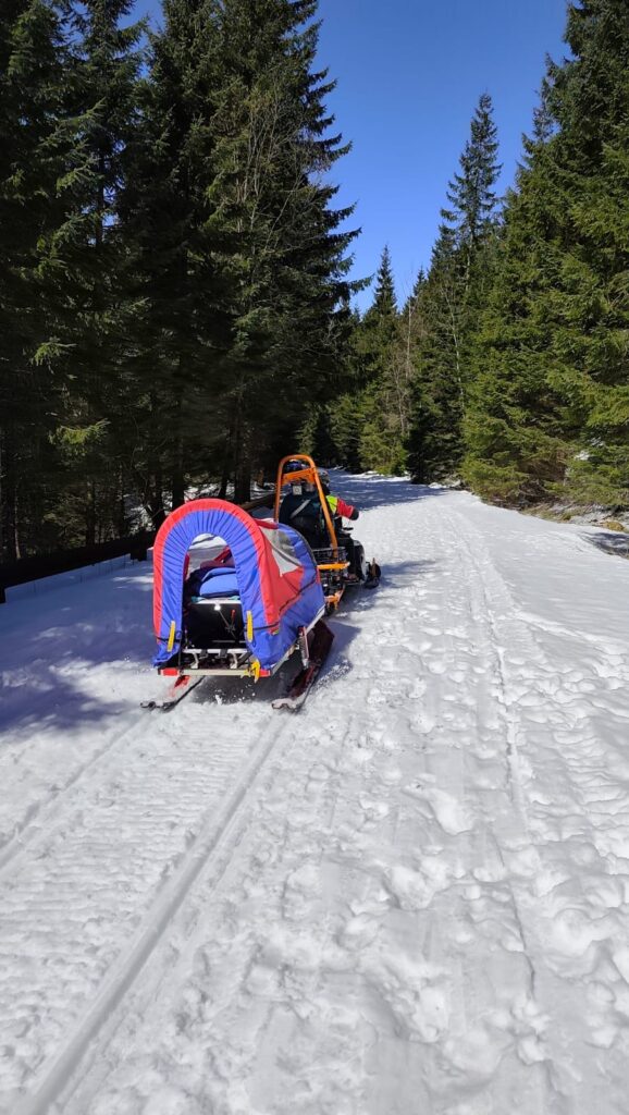 Záchranári HZS pomocou nosidiel pripojených za skútrom transportujú po zasneženej ceste turistku so žalúdočnými kŕčmi