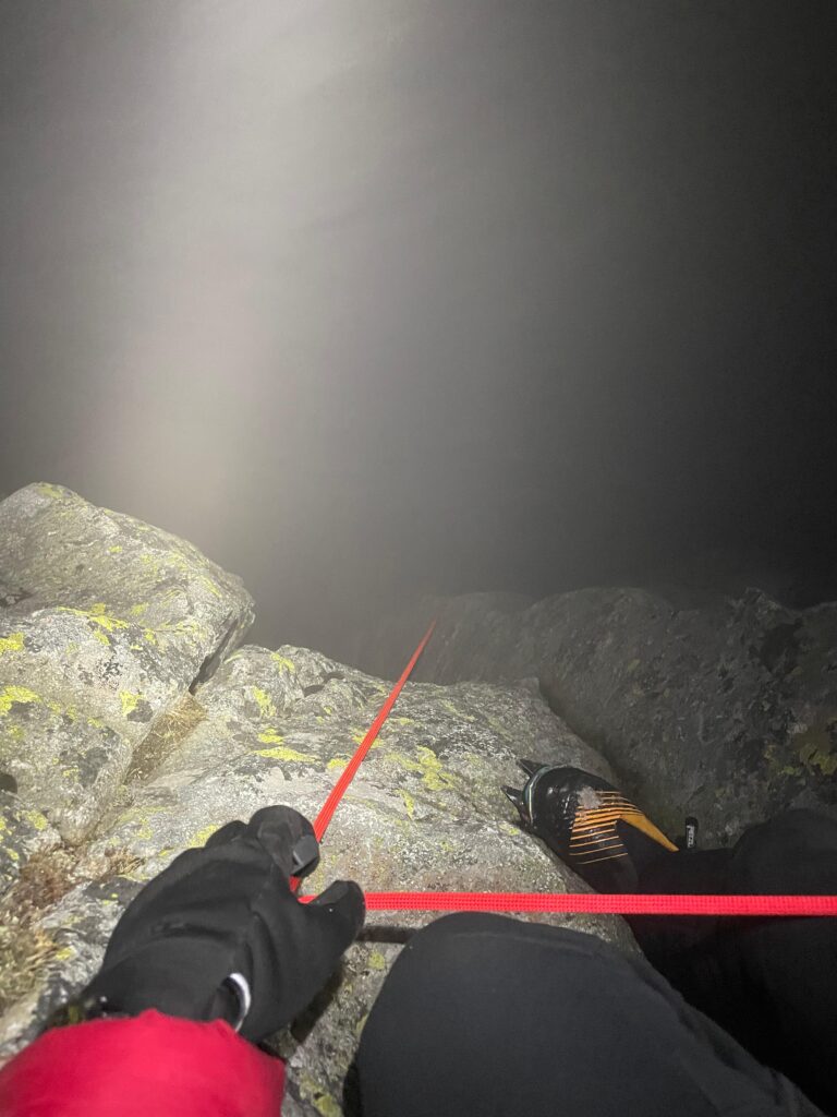 fotka z pohľadu záchranára HZS - rukou drží červené istiace lano, obuté vysokohorské topánky a na nich mačky a pod ním hustá hmla 