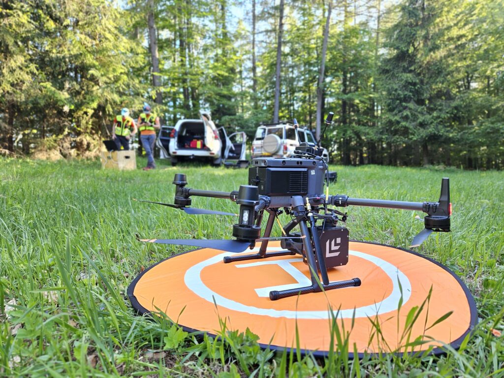 Dron vybavený zariadením na vyhľadávanie mobilných telefónov na lúke v pozadí s terénnymi vozidlami HZS