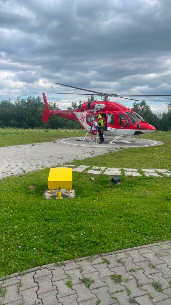 vrtuľník VZZS na heliporte v Starom Smokovci, z ktorého vystupuje záchranár HZS s vyprosteným mužom