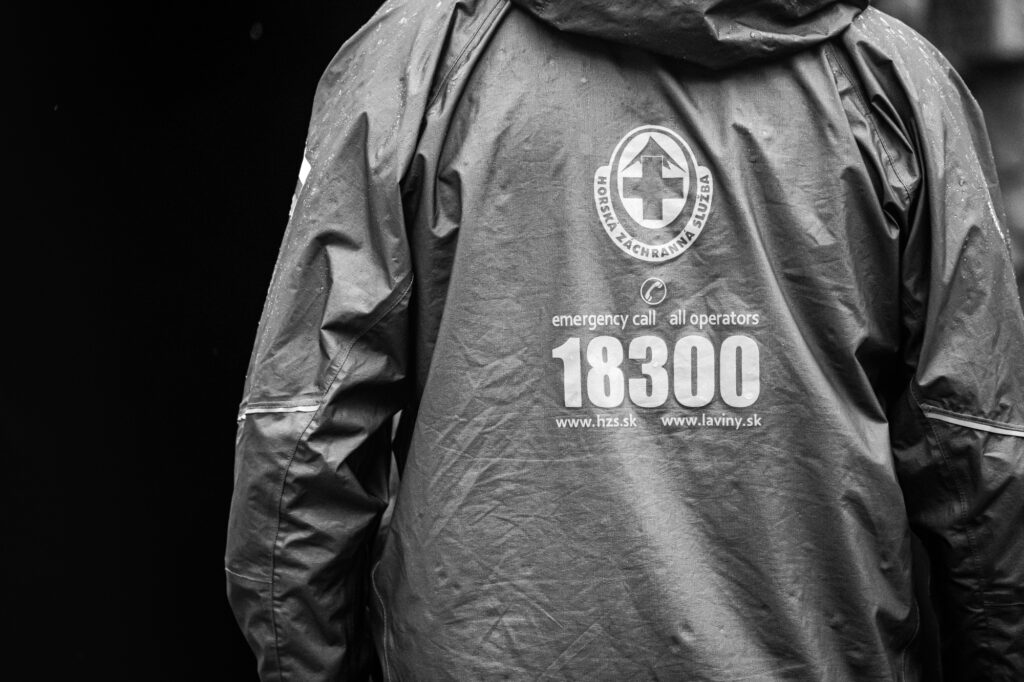 ilustračná foto - záchranár HZS v sivej bunde, na chrbte logo HZS a 18 300, čierne pozadie