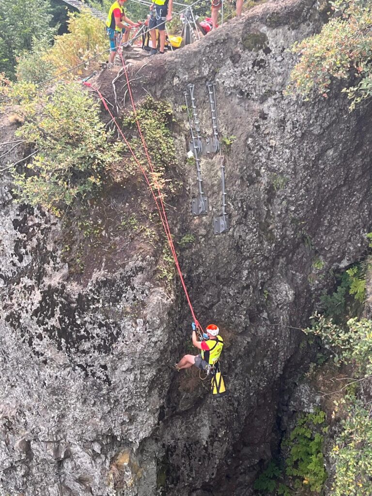 záchranár HZS je spúšťaný kolegom pomocou lanovej techniky k zranenému lezcovi na ferrate