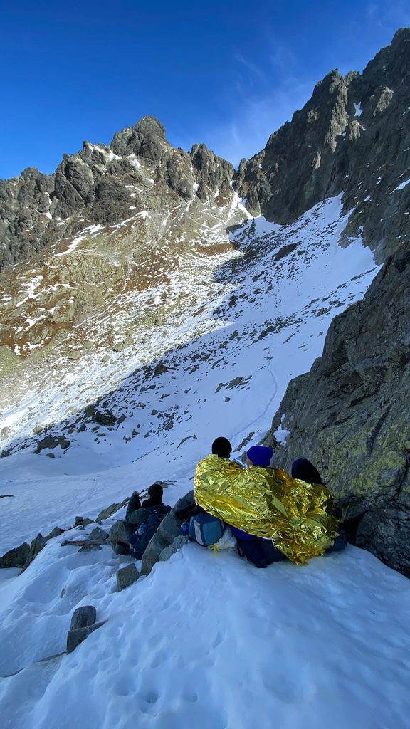 Turisti sediaci na kameni v zasneženej časti doliny prikrytí izotermickou fóliou